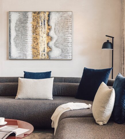 Ein modernes Sofa mit Kissen steht unter einem gerahmten Kunstbild an einer hellen Wand.