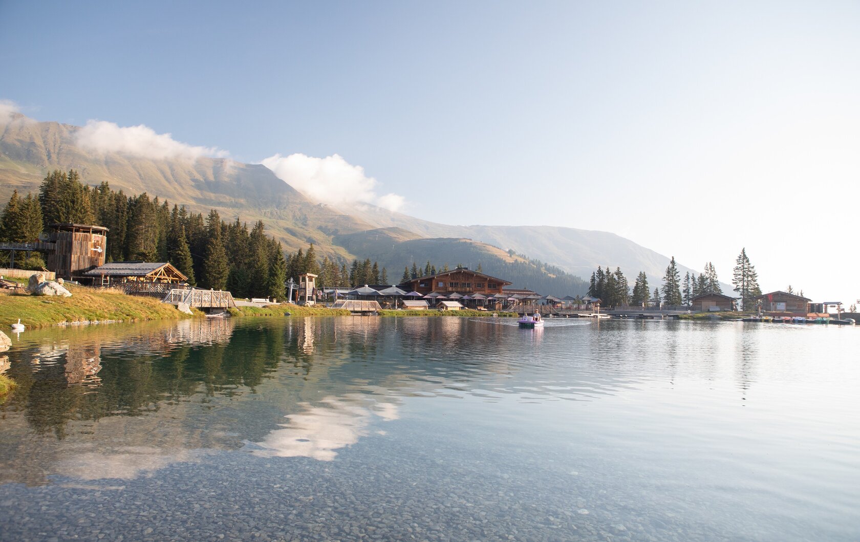 Bergsee mit Alpenhütte in Fiss Ein ruhiger Bergsee mit Holzhütten, Wäldern und Bergen im Hintergrund.