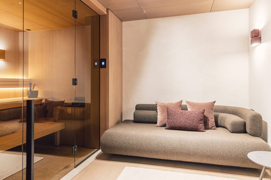 Ein Wohnbereich mit Sofa und Glaswand neben der Sauna in einem stilvoll gestalteten Apartment.