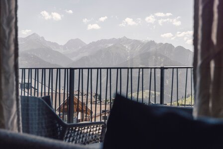 Blick vom Apartmentbalkon auf die Berge und Dächer in Fiss, mit Geländer im Vordergrund.