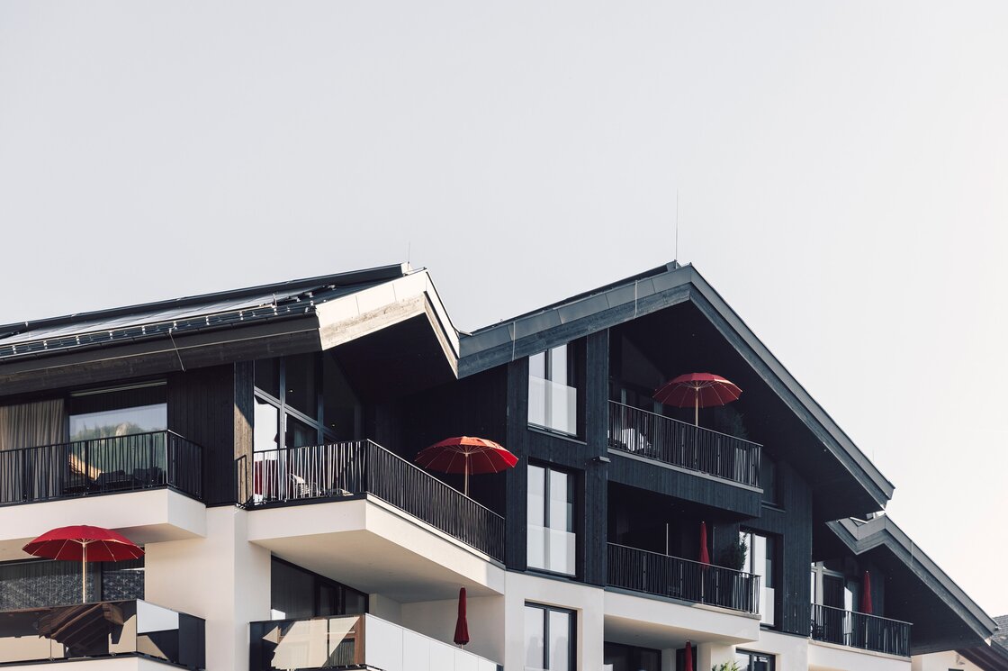 Außenansicht von Domenig's Luxury Apartments mit mehreren Balkonen und roten Sonnenschirmen.
