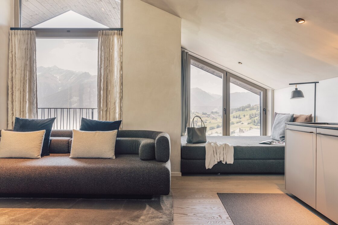 Ein moderner Wohnbereich mit Sofa, Schlafnische und großen Fenstern mit Blick auf die Berge.