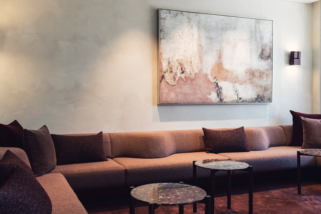 Ein gemütlicher Lounge-Bereich mit Sofa, kleinen Tischen und großem Wandbild.