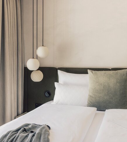 Ein modern eingerichtetes Schlafzimmer mit Doppelbett, Hängelampen und Vorhängen neben einer hellen Wand.