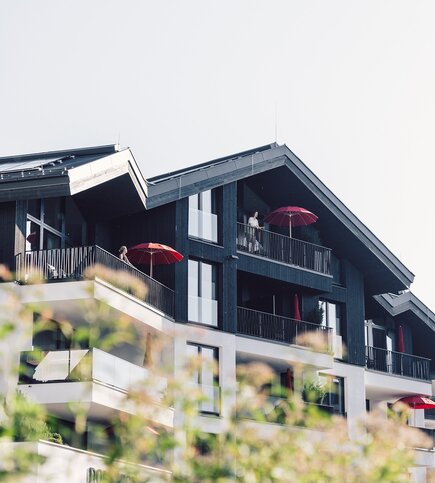 Ein modernes Apartmenthaus mit Balkonen und roten Sonnenschirmen vor hellem Himmel.