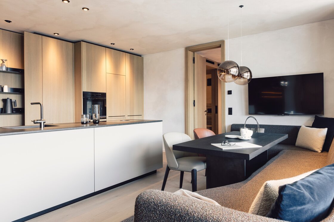 Offener Küchen- und Wohnbereich eines Luxusapartments mit Esstisch, Sofa und moderner Einbauküche.