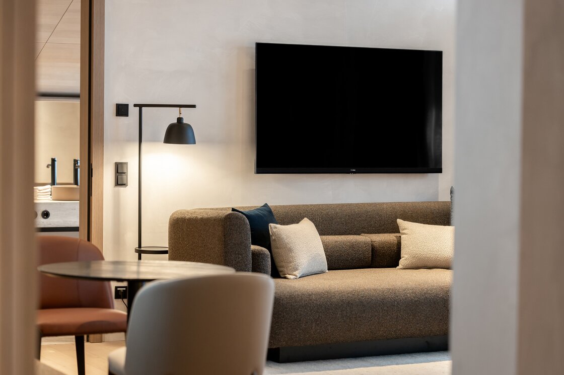Ein moderner Wohnbereich mit Sofa, Stehleuchte und großem Wandfernseher.