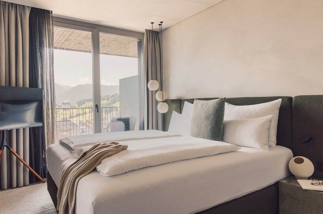 Ein Schlafzimmer mit Doppelbett und Blick auf die Berge durch große Glasfenster.