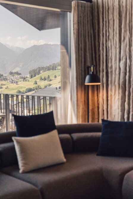 Ein Wohnbereich mit Sofa und Kissen bietet Blick auf die grünen Berge und Dächer von Fiss.