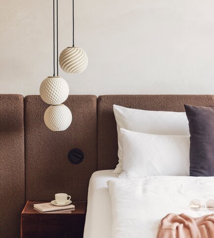 Ein stilvoll gestaltetes Schlafzimmer mit Bett, Kopfteil, Nachttisch und drei Hängelampen.