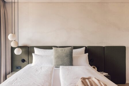 Ein modernes Schlafzimmer mit Doppelbett, gepolstertem Kopfteil und drei Hängelampen neben dem Fenster.