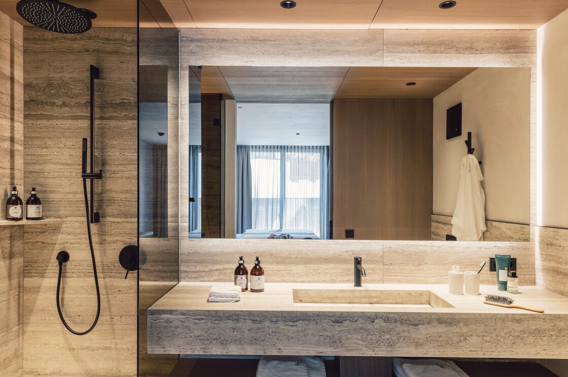 Modernes Badezimmer mit Regendusche, großem Spiegel und Steinoptik im Apartment in Fiss.