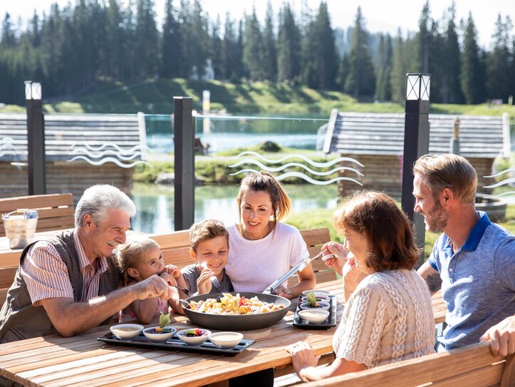 Familienessen auf der Terrasse in Fiss Eine Familie sitzt auf einer Terrasse am See und isst gemeinsam in der Sonne.