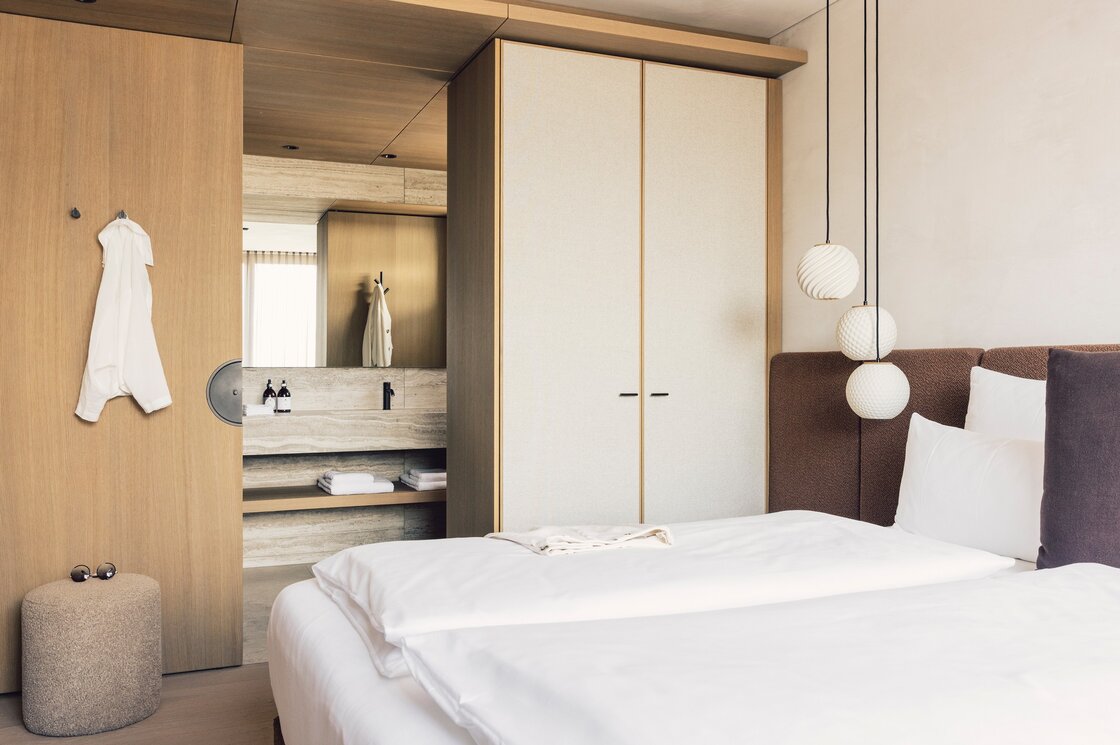 Ein modernes Schlafzimmer mit Doppelbett, Einbauschrank und offenem Badbereich.