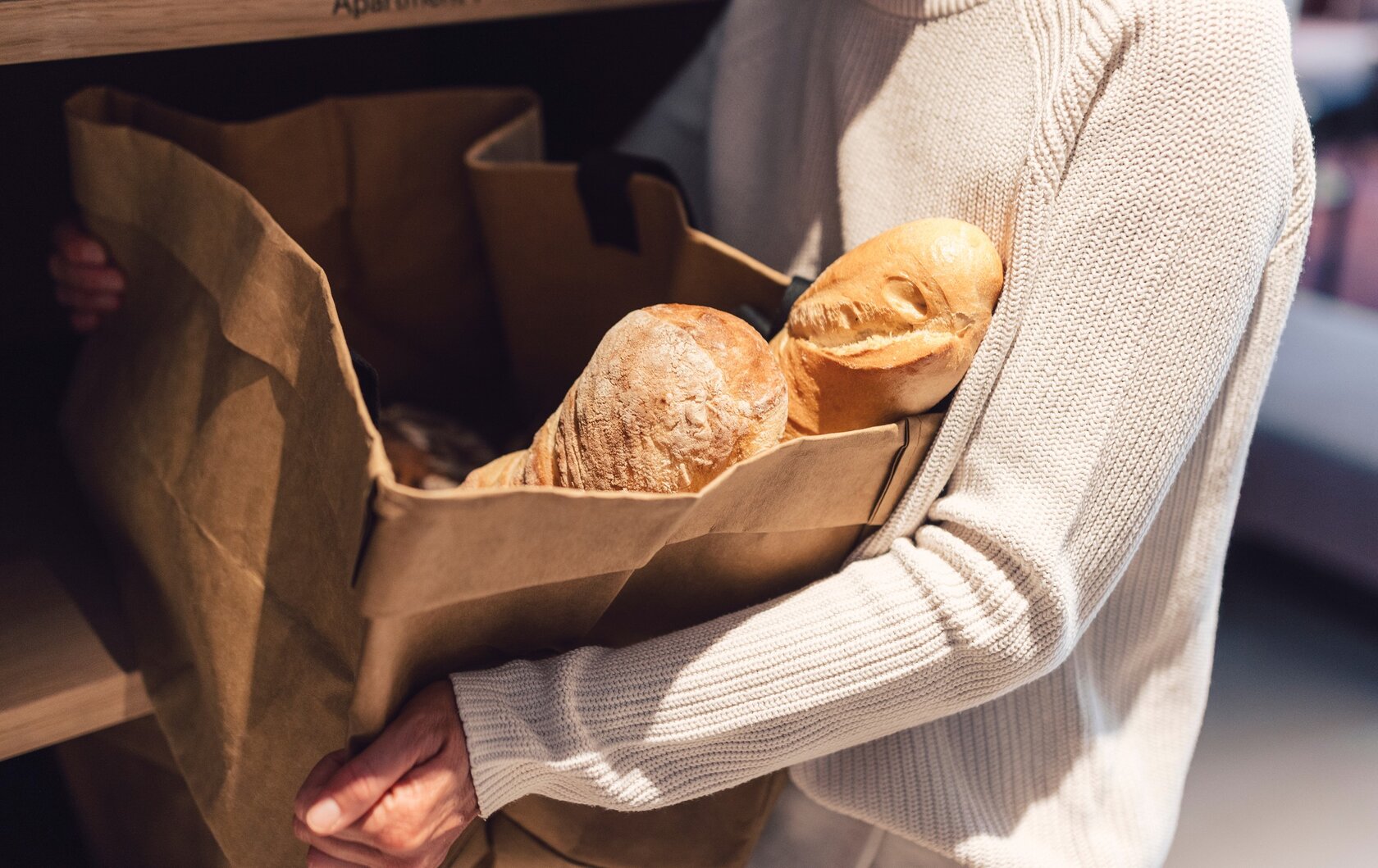 Eine Person trägt einen Papierbeutel mit frischem Brot im Innenbereich.