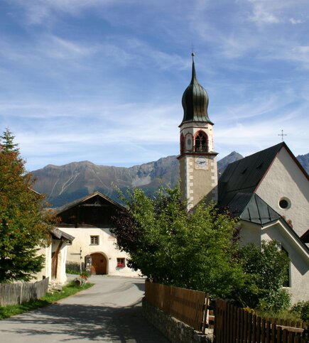 Eine Dorfkirche mit Kirchturm steht vor der Bergkulisse in Fiss.