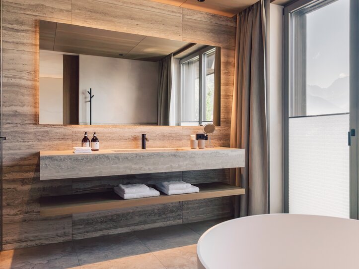 Ein modernes Badezimmer mit Waschtisch, großem Spiegel und Blick durch das Fenster auf die Berge.