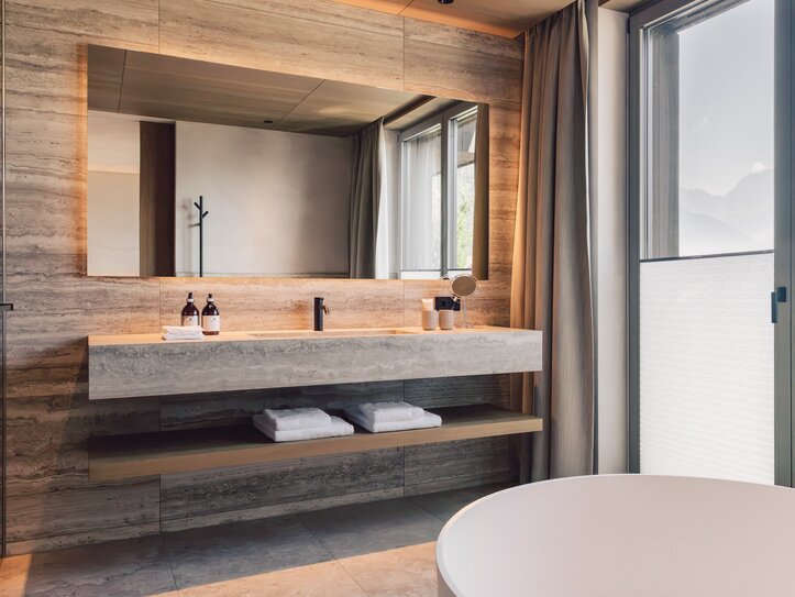 Ein modernes Badezimmer mit Waschtisch, großem Spiegel und Blick durch das Fenster auf die Berge.