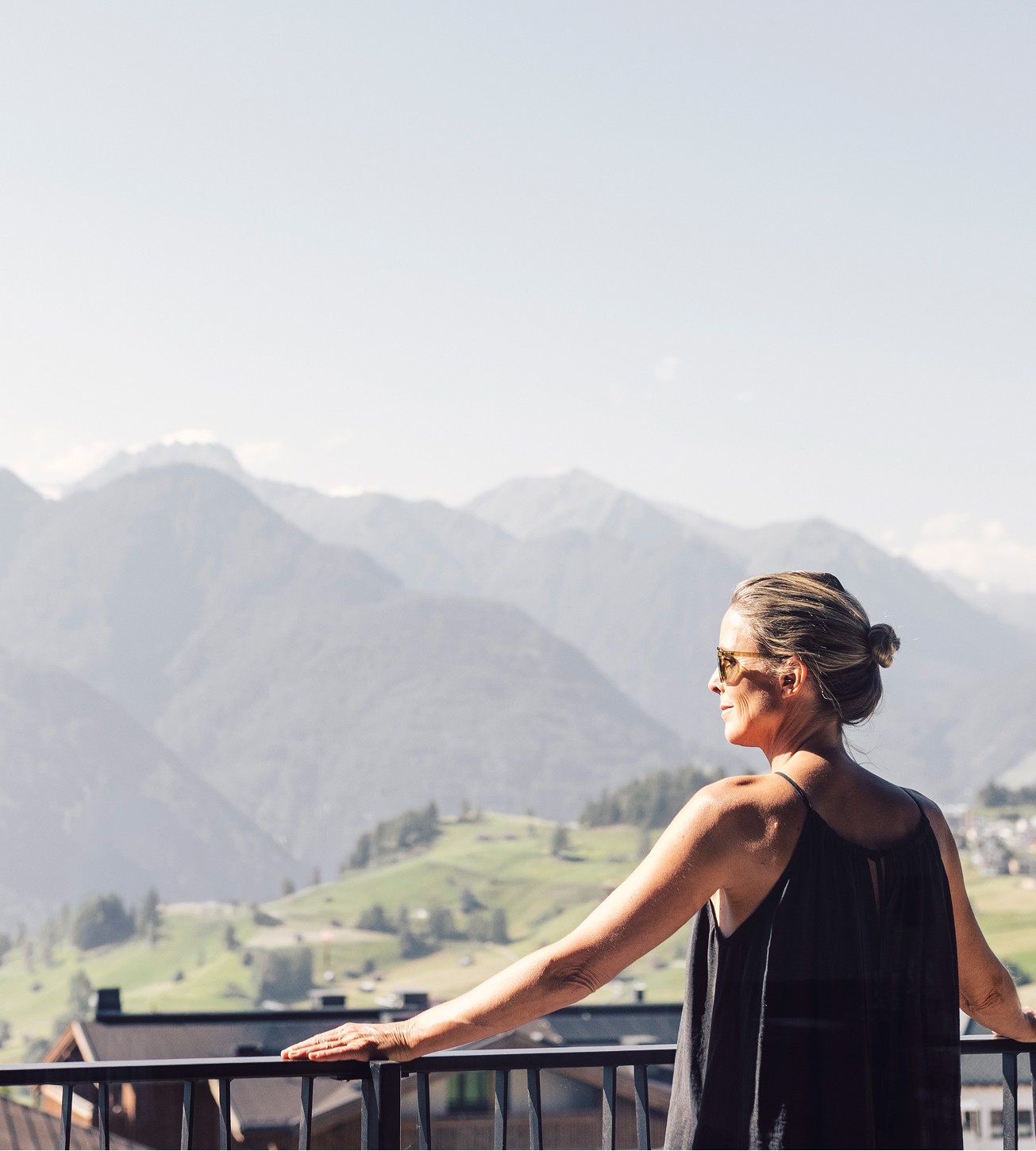 Eine Frau lehnt am Balkon und blickt über die grünen Berge und Täler.