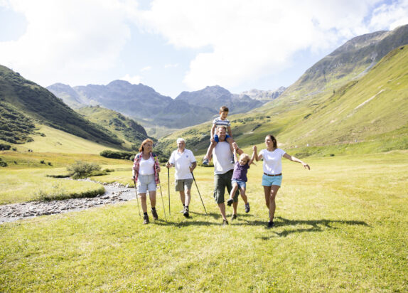 Wandern in Serfaus Fiss Ladis, Familie läuft über eine Wiese, Berge im Hintergrund