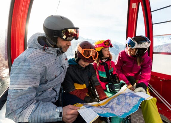 Familie sitzt in Gondel im Fiss Skigebiet und liest einen Pistenplan