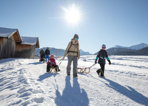 Insider tip for skiing holidays with children, family pulls a toboggan behind them