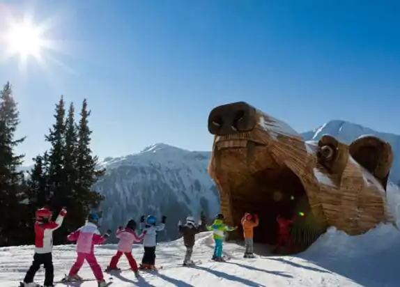 Skigebiet für Familien, Bärenpiste in Serfaus, Kinder fahren Ski durch einen Bären aus Holz