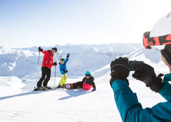 Skiurlaub mit Kindern, Papa macht Foto von Mama und zwei Kindern, Berge und Schnee im Hintergrund