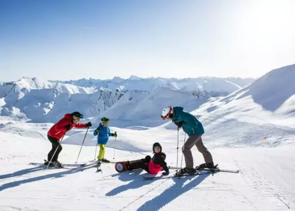 Skiurlaub mit Kindern, Familie steht mit Ski- und Snowboardausrüstung auf der Piste, Berge und Schnee im Hintergrund