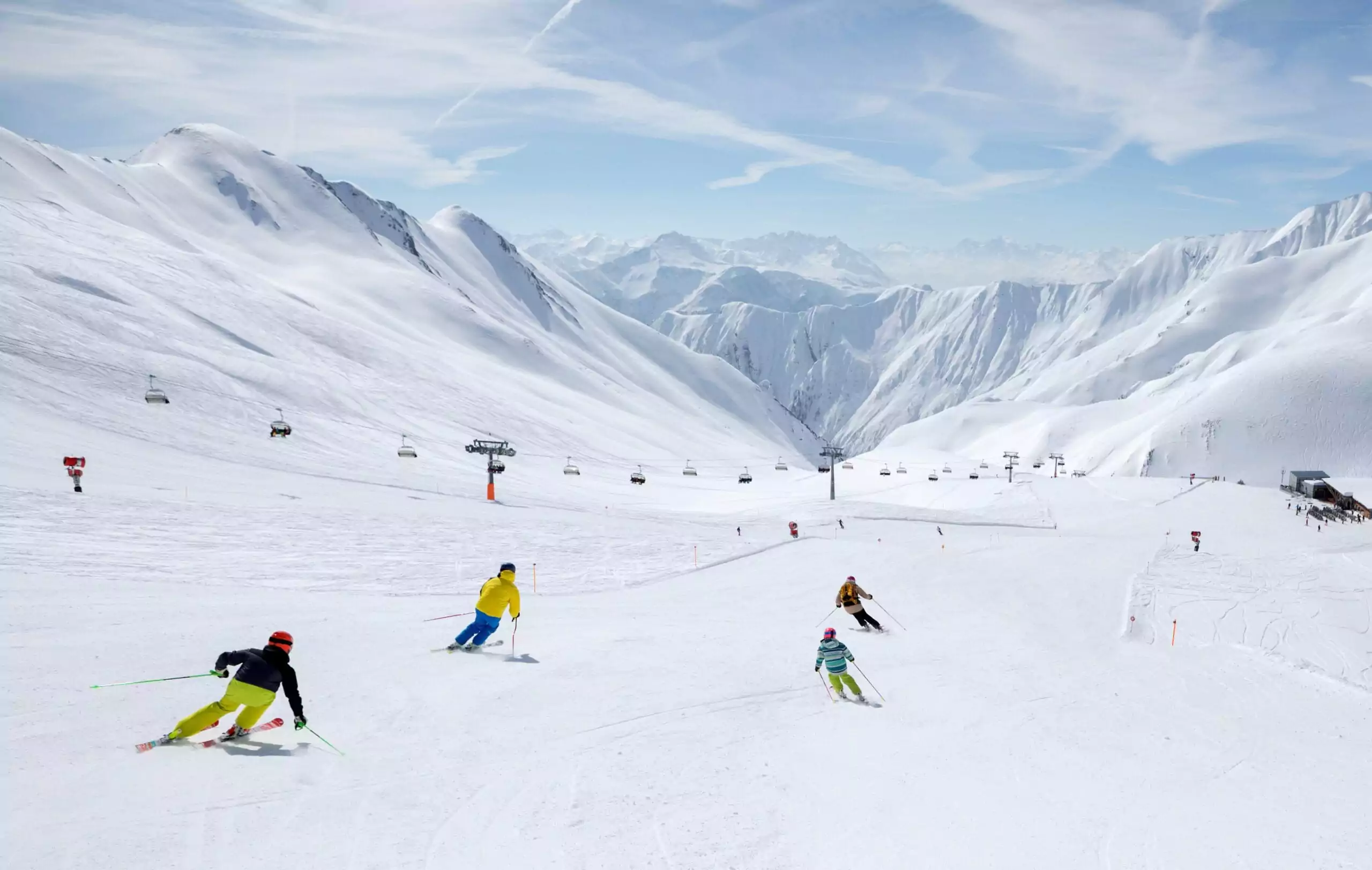 Skigebiet für Familien, Familie fährt Ski auf einer breiten weißen Skipiste, links ist ein Sessellift