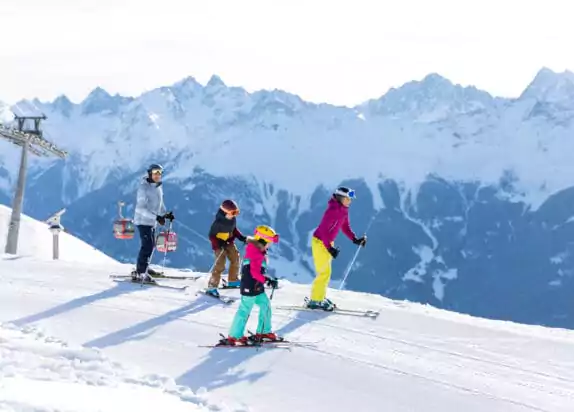 Familienskiurlaub, Familie fährt auf einer flachen Poste Ski, Berge im Hintergrund