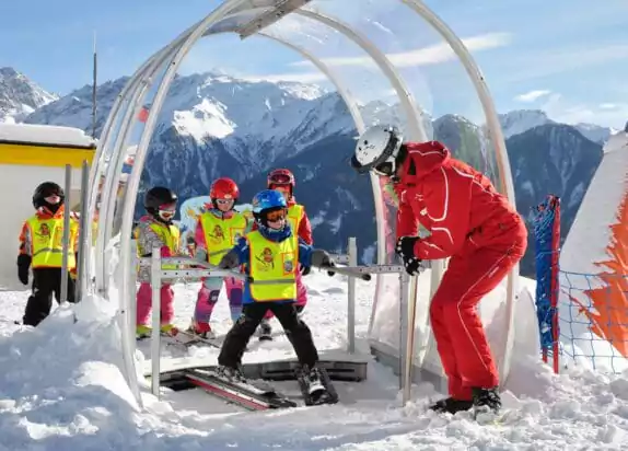 Familienurlaub Berge, Übungslift Kinder stehen an, Skilehrer erklärt was