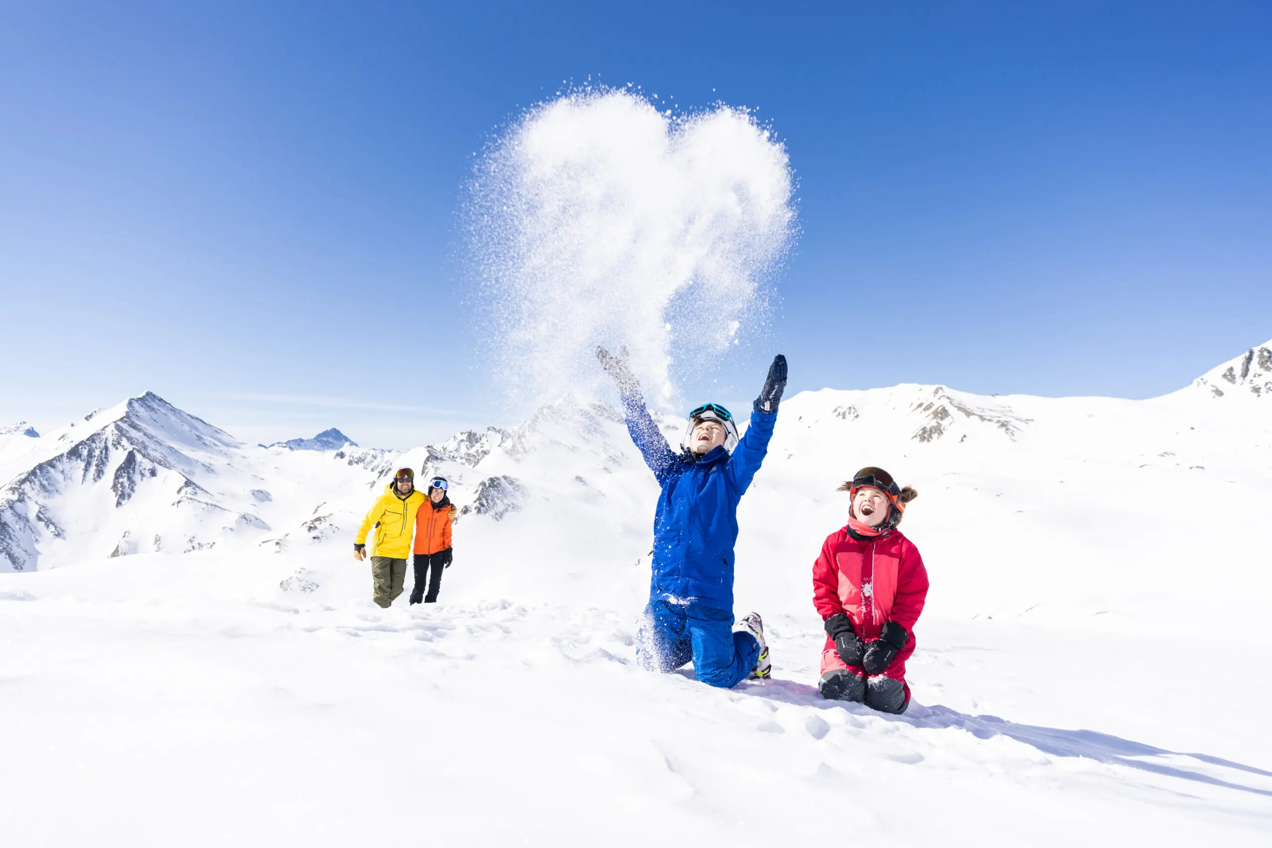 Insider tip for skiing vacations with children - children throw snow up in the air, parents in the background